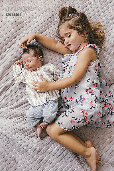 Girl lying on blanket cuddling with her baby brother