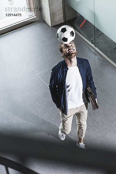 Casual young businessman playing football in office