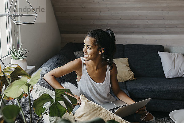 Young woman sitting with laptop on the couch looking out of window