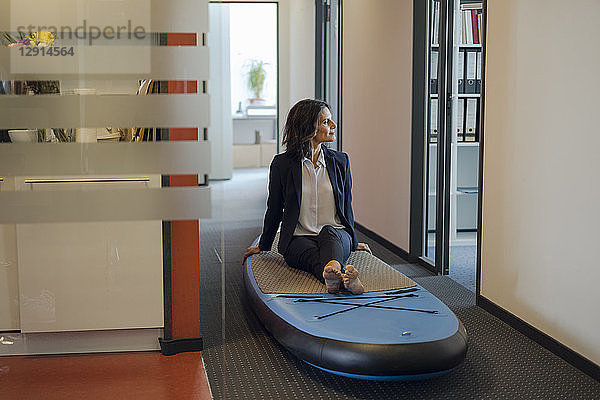 Businesswoman sitting on paddle board  daydreaming in office