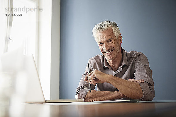 Portrait of confident mature man with laptop and documents at home