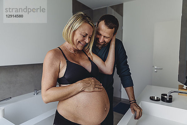 Happy mature pregnant couple watching expectant mother?s belly in bathroom