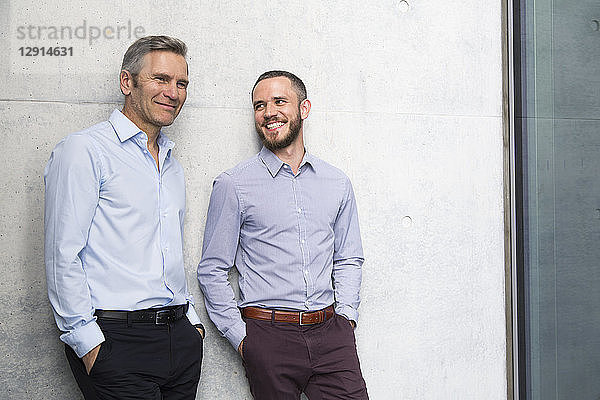 Portrait of two smiling businessmen at a wall