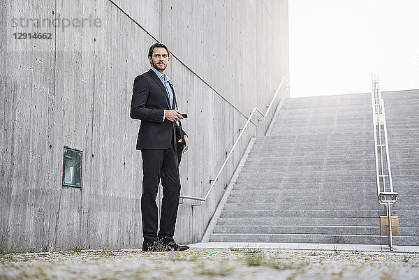 Businessman standing at stairs holding smartphone