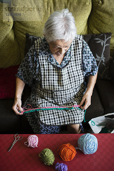 Senior woman crocheting on the couch at home  top view