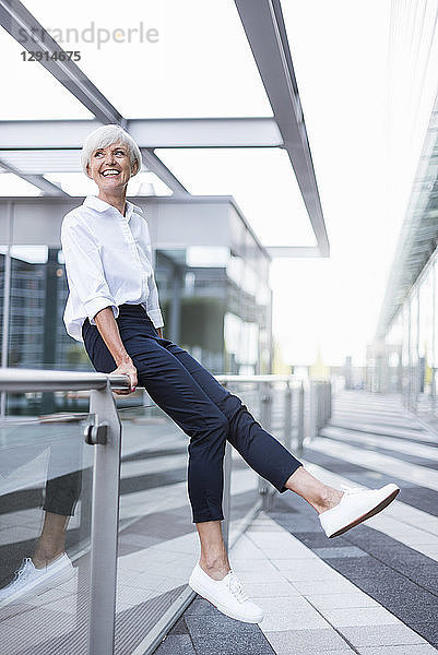 Happy senior woman sitting on railing in the city looking around