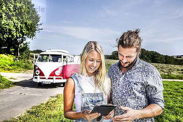 Happy couple outside van in rural landscape looking at tablet