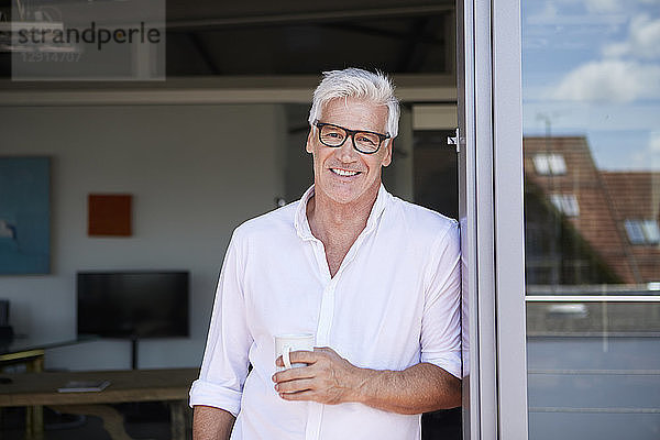 Portrait of smiling mature man holding coffee cup at the balcony at home