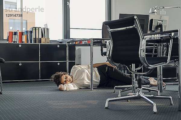 Tired businesswoman sleeping on floor under her desk