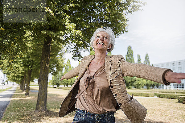 Happy senior woman with outstretched arms in a park