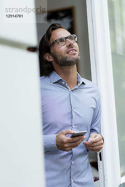 Confident man standing in doorframe holding cell phone looking up