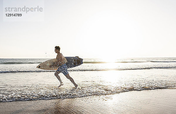 Young man running on beach  carrying surfboard