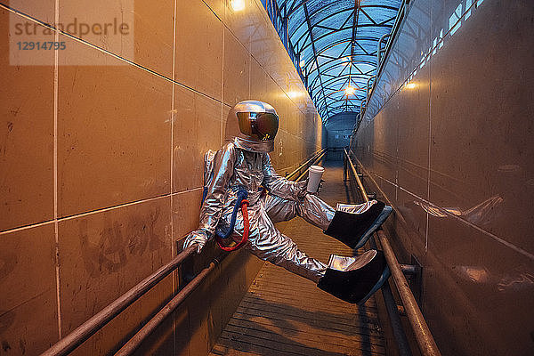 Spaceman in the city at night with takeaway coffee in narrow passageway