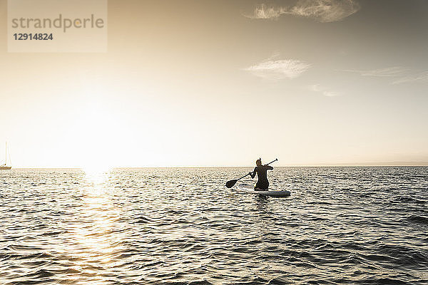 Young woman stand up paddle surfing at sunset