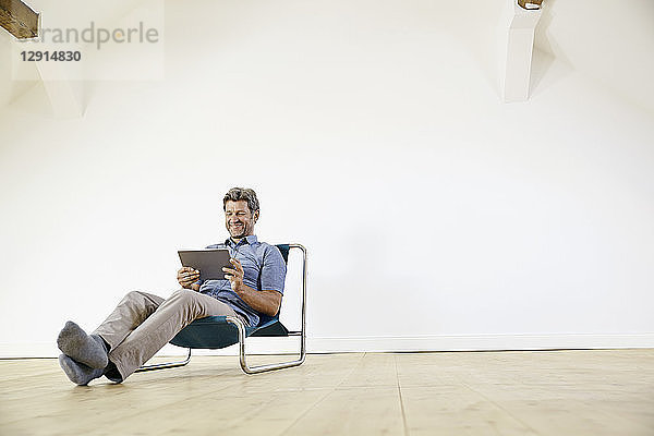 Man sitting in arm chair  using digital tablet