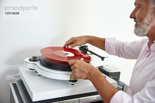 Mature man putting red vinyl record on record player