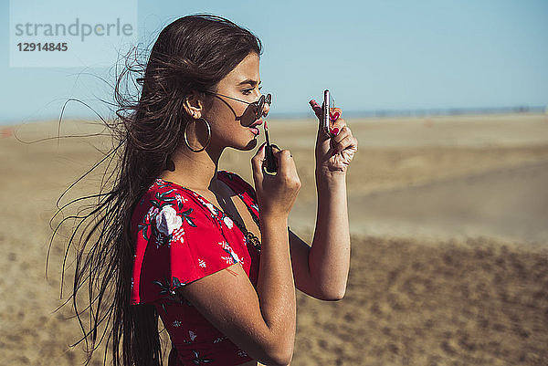 Teenage girl applying lip gloss on the beach