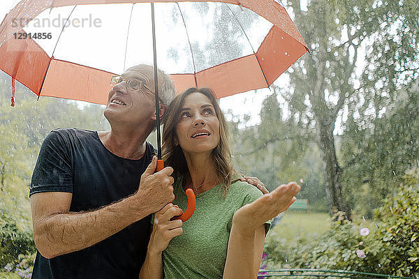 Smiling mature couple standing in rain under umbrella