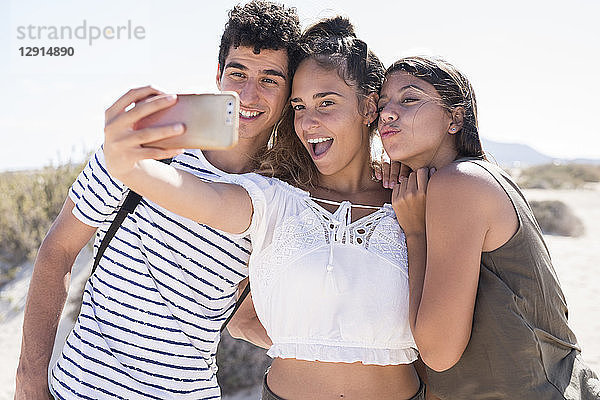Friends having fun on the beach  taking smartphone selfies