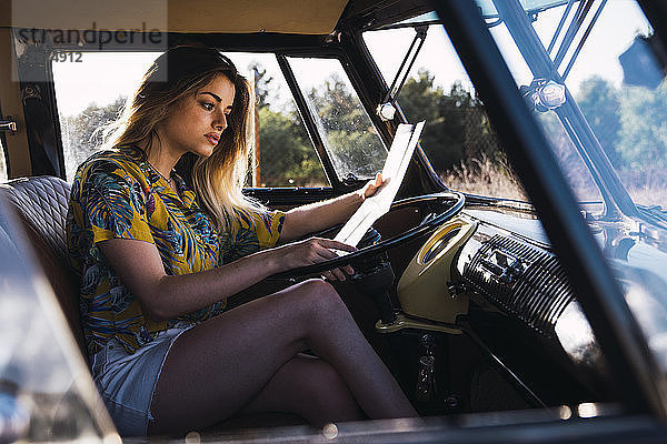 Young woman sitting in a van reading map