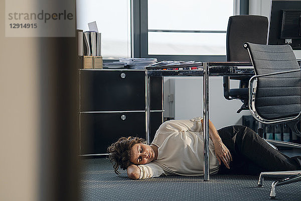Tired businesswoman sleeping on floor under her desk