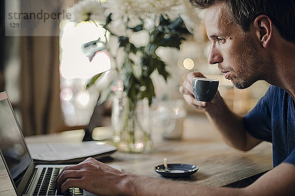 Mid adult man sitting in coffee shop  drinking coffee  using laptop