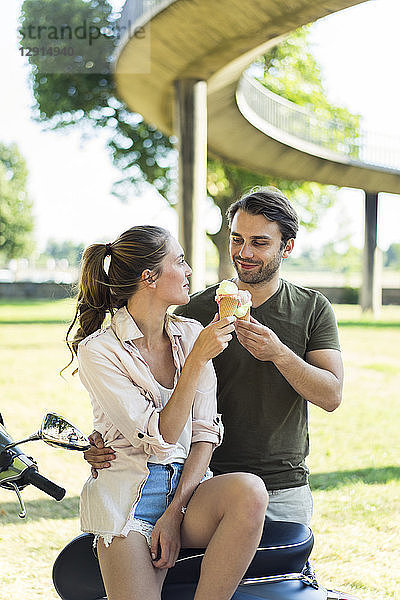 Smiling couple with motor scooter in summer eating ice cream