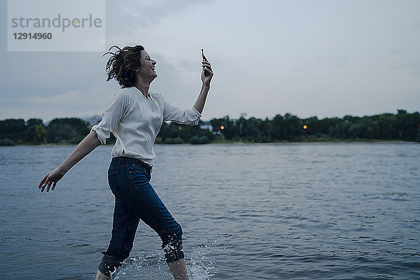 Laughing woman running at the riverside  using smartphone