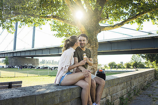 Happy couple sitting on a wall in summer eating ice cream