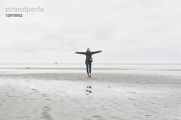 Netherlands  Ouddorp  back view of woman with arms outstretched standing on the beach in autumn
