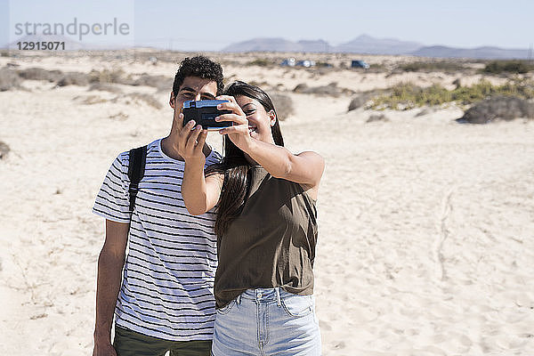 Young couple having fun on the beach  taking smartphone selfies