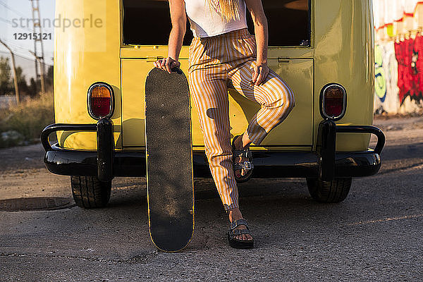 Young woman with skateboard standing outside at a vintage van
