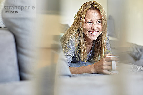 Laughing young woman relaxing on couch  drinking coffee