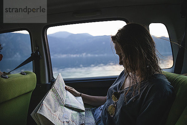 Young woman sitting on backseat in a car looking at map