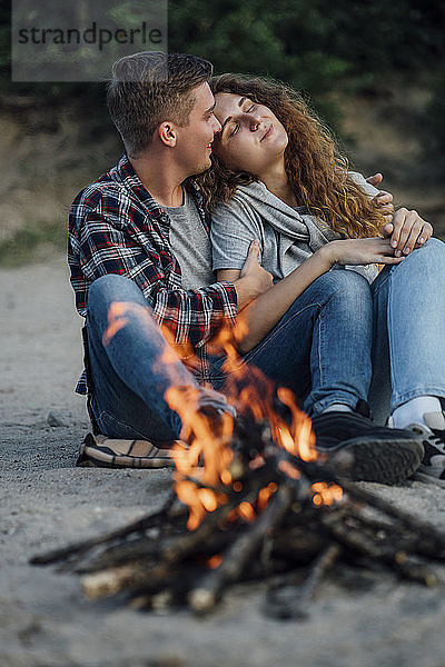 Romantic couple sitting at a campfire at he riverside