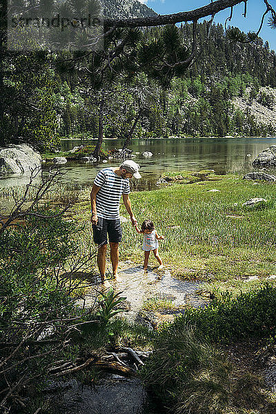 Spain  Father and daughter exploring mountain lake  standing ankle deep in water