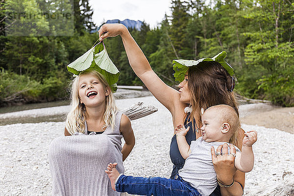 Mother with two children playing with leaves at the riverside