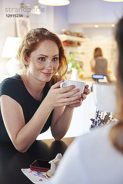 Smiling young woman drinking coffee with friend at cafe