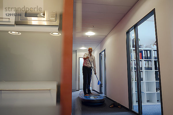 Businessman standing on paddle board  exercising in office corridor