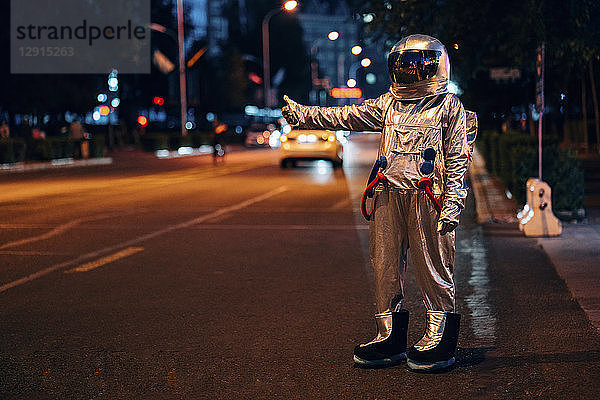 Spaceman standing on a street in the city at night hitchhiking