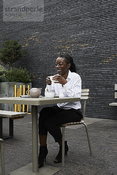 Laughing businesswoman sitting on terrace of a coffee shop drinking tea