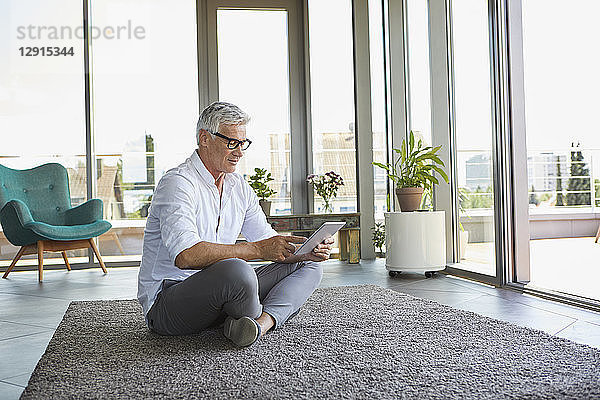 Mature man sitting on carpet at home using tablet