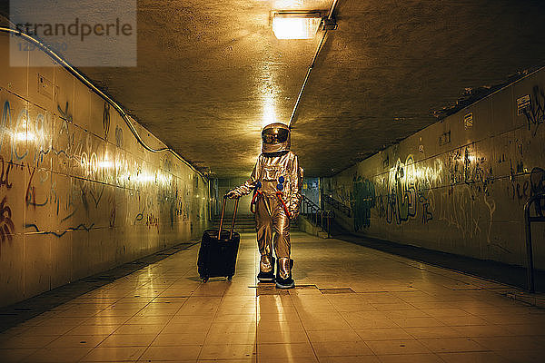 Spaceman in the city at night in underpass with rolling suitcase