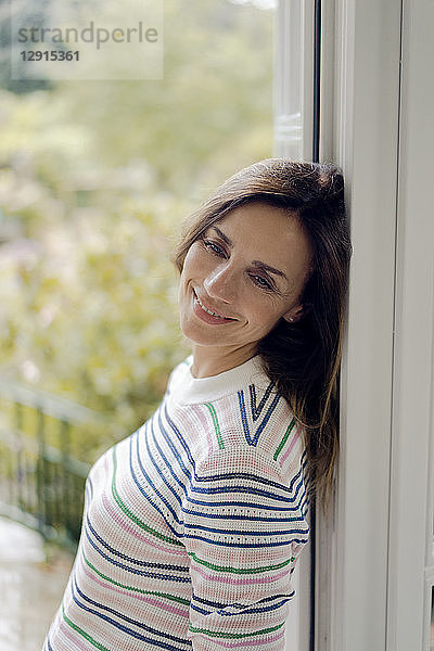 Portrait of smiling mature woman leaning against terrace door at home