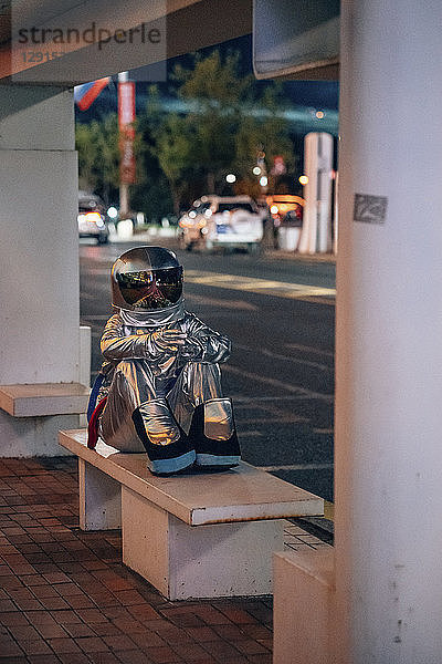 Spaceman sitting on bench at a bus stop at night