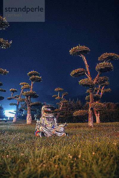Spaceman in yoga pose siting in a park at night