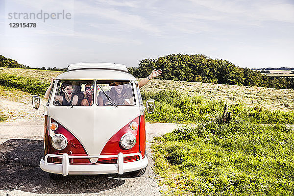 Happy friends inside van in rural landscape