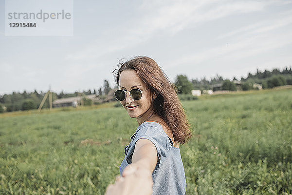 Smiling woman wearing sunglasses holding hand of partner in rural field