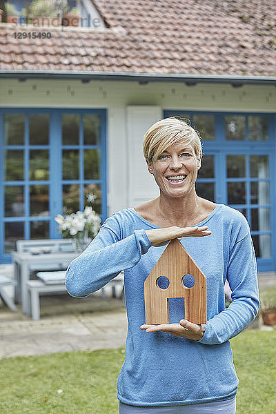 Portrait of smiling woman standing in front of her home holding house model