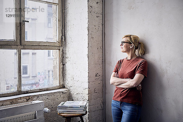 Smiling woman leaning against wall in loft looking through window